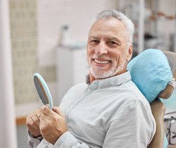 patient smiling while holding dental mirror 