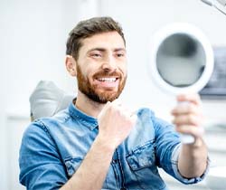 man admiring his smile in mirror after seeing cosmetic dentist in State College