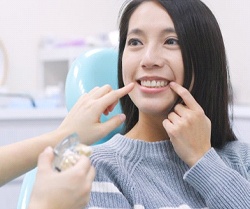 A dental patient smiling while cosmetic dentist points at her mouth