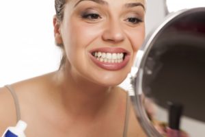 young woman looking at her teeth in a mirror 