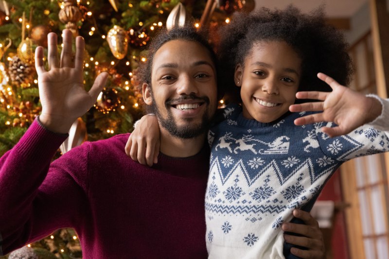 Man with his child smiling and waving in front of Christmas tree