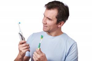 A man comparing electric and manual toothbrushes.