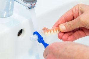 Person cleaning denture with toothbrush